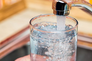 A glass cup being filled with tap water from a sink